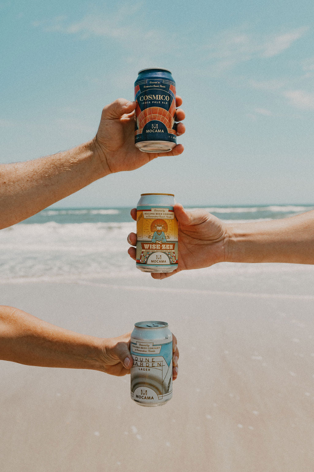 Friends holding Mocama cans together by the ocean