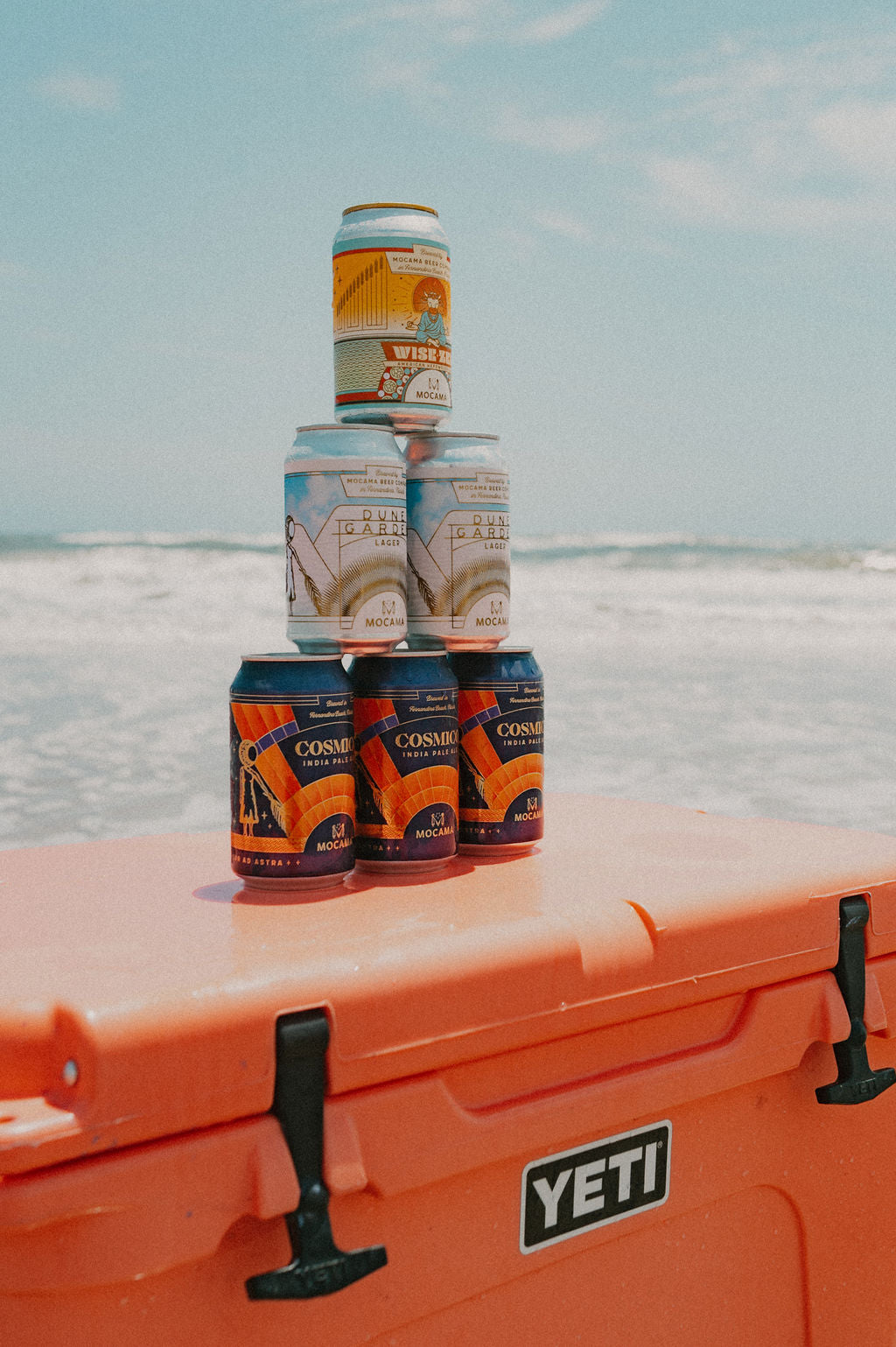 Mocama cans stacked on an orange cooler at the beach