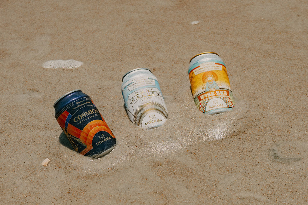 Cosmico, Dune Garden and Wise-Zen cans resting in the sand