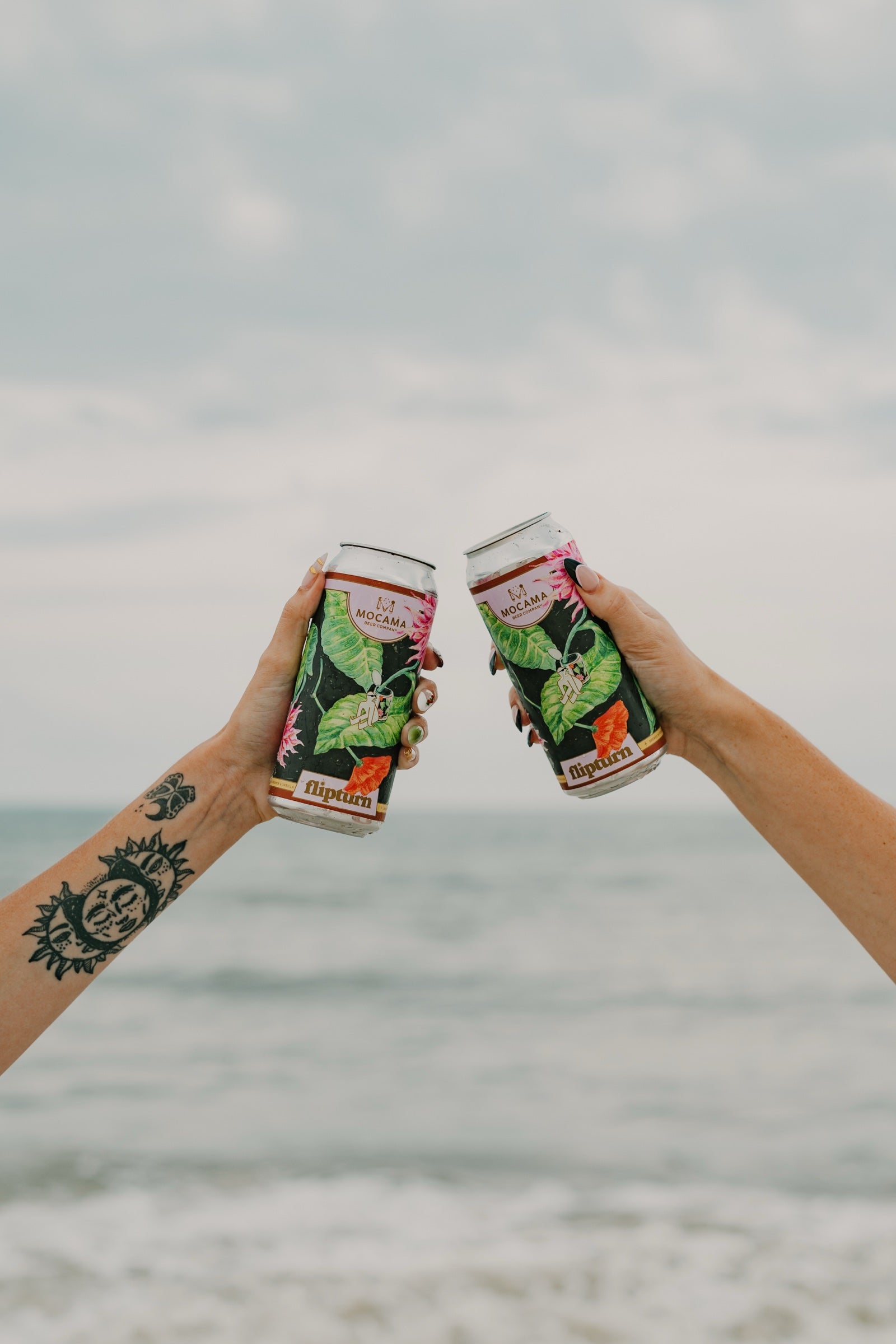 Two people toasting flipturn cans at the beach